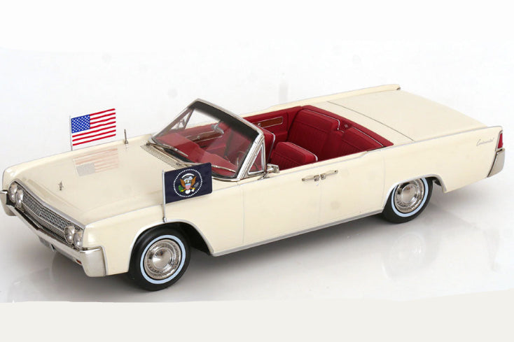 A cream-colored vintage convertible car model with a red interior, featuring a small American flag and a presidential emblem on the windshield, set against a plain white background.